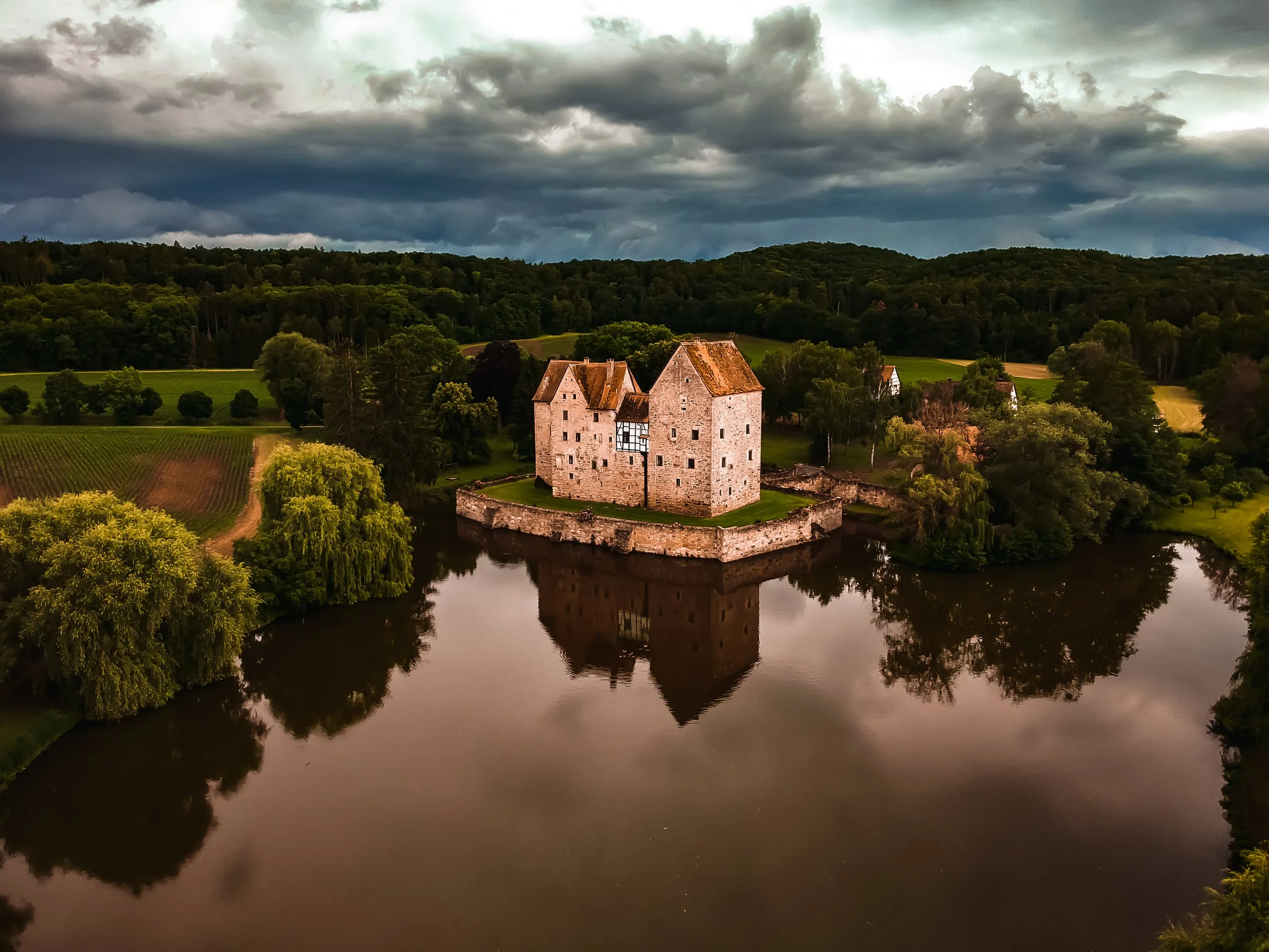 The moated castle of Brennhausen on its small island in a pond, storm clouds above