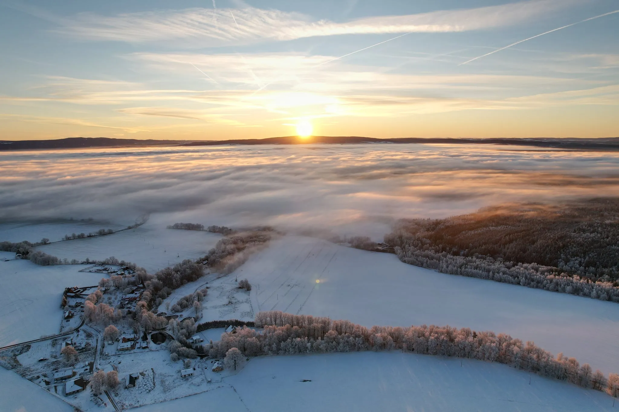 Sunrise over a sea of fog on Zelená hora, a snowy village in hoarfrost in the foreground