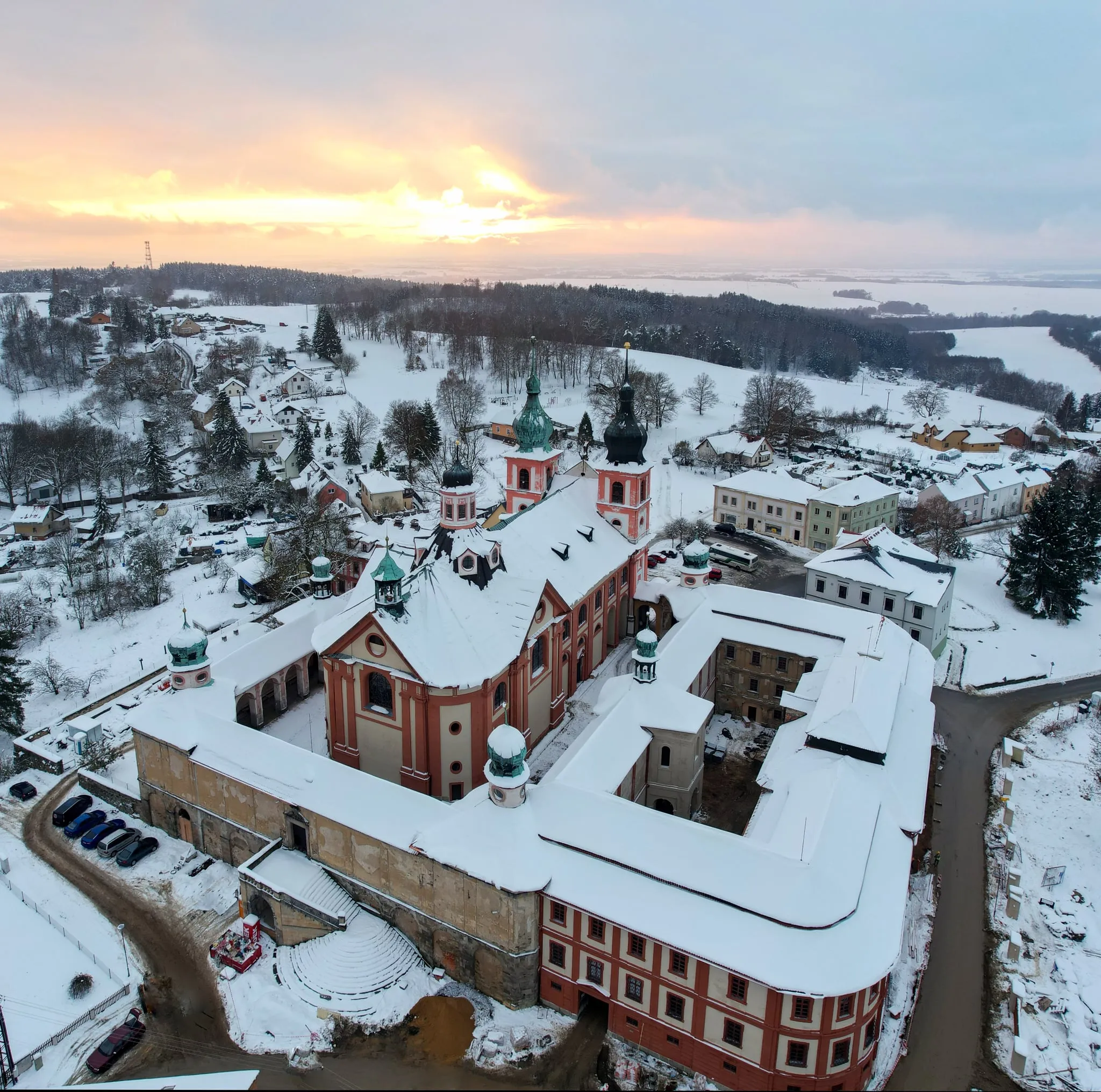 Klášter s kostelem v Chlumu Svaté Maří pod sněhem, nízké slunce nad obzorem
