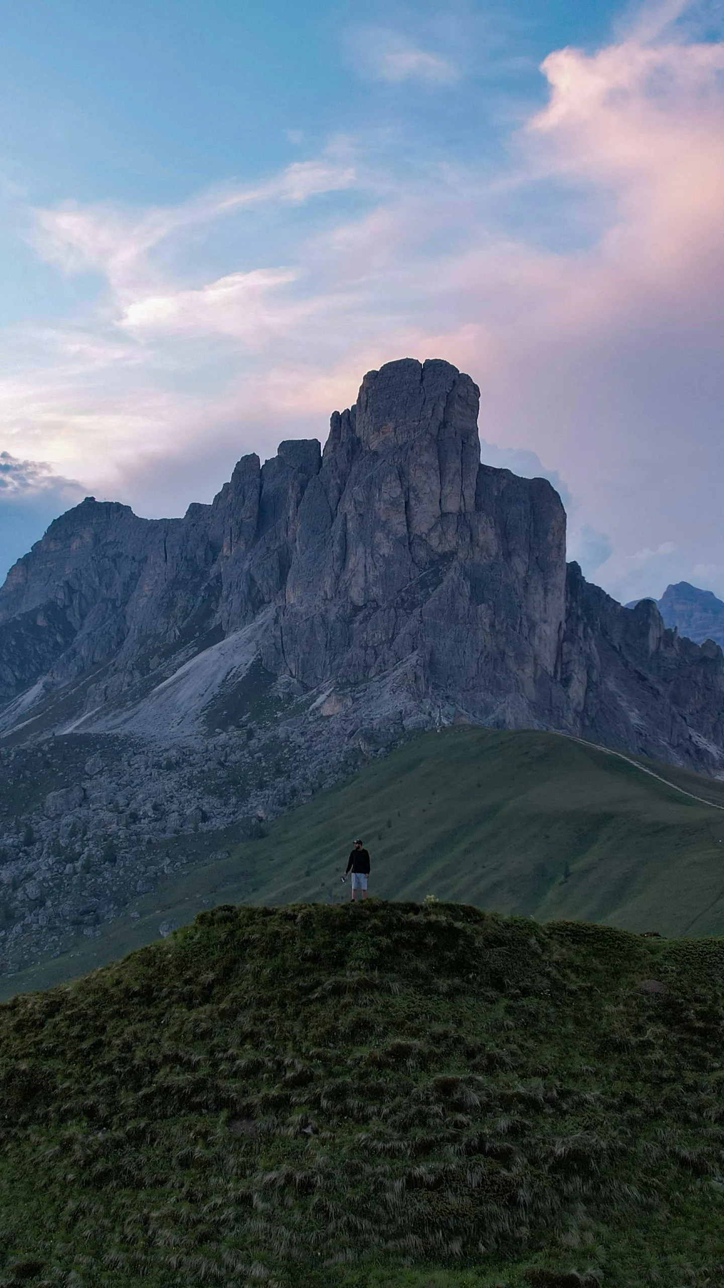A rock tower above the grassy saddle of Passo Giau, pink clouds at sunset