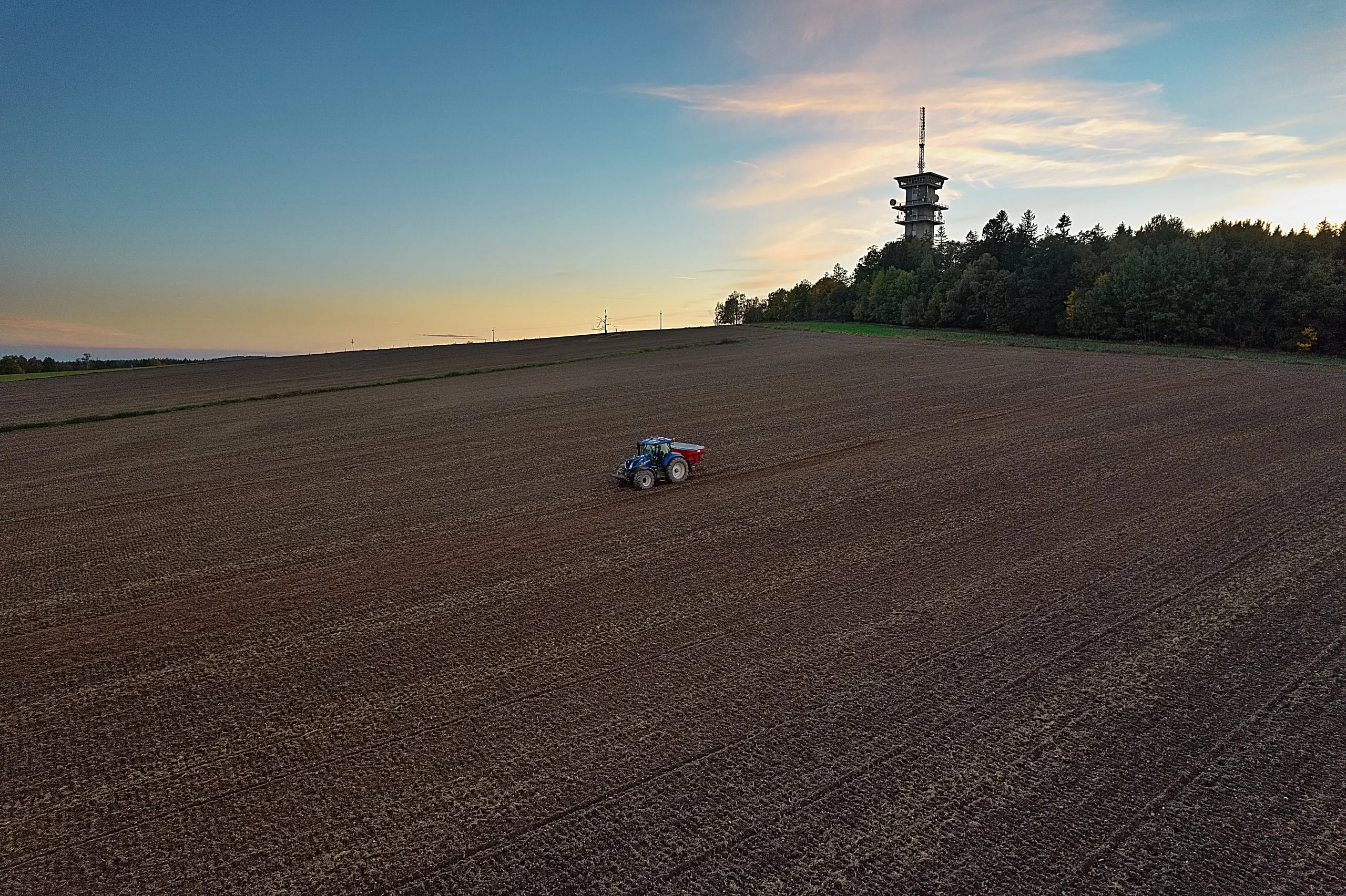 A tractor on a ploughed field, the lookout tower on Zelená hora on the horizon