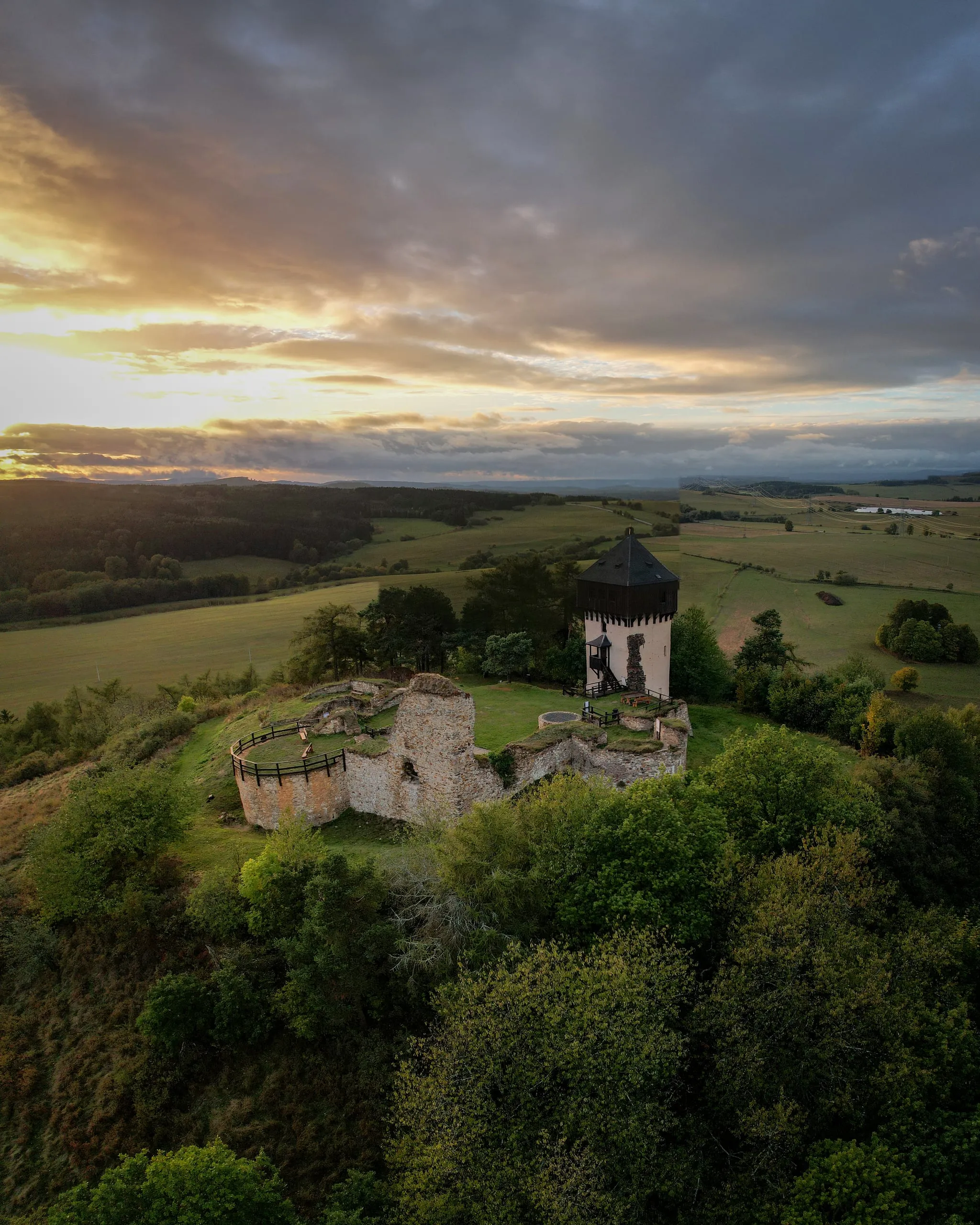 The ruins of Hartenštejn Castle near Bochov, with a round tower on a wooded hill in the afterglow