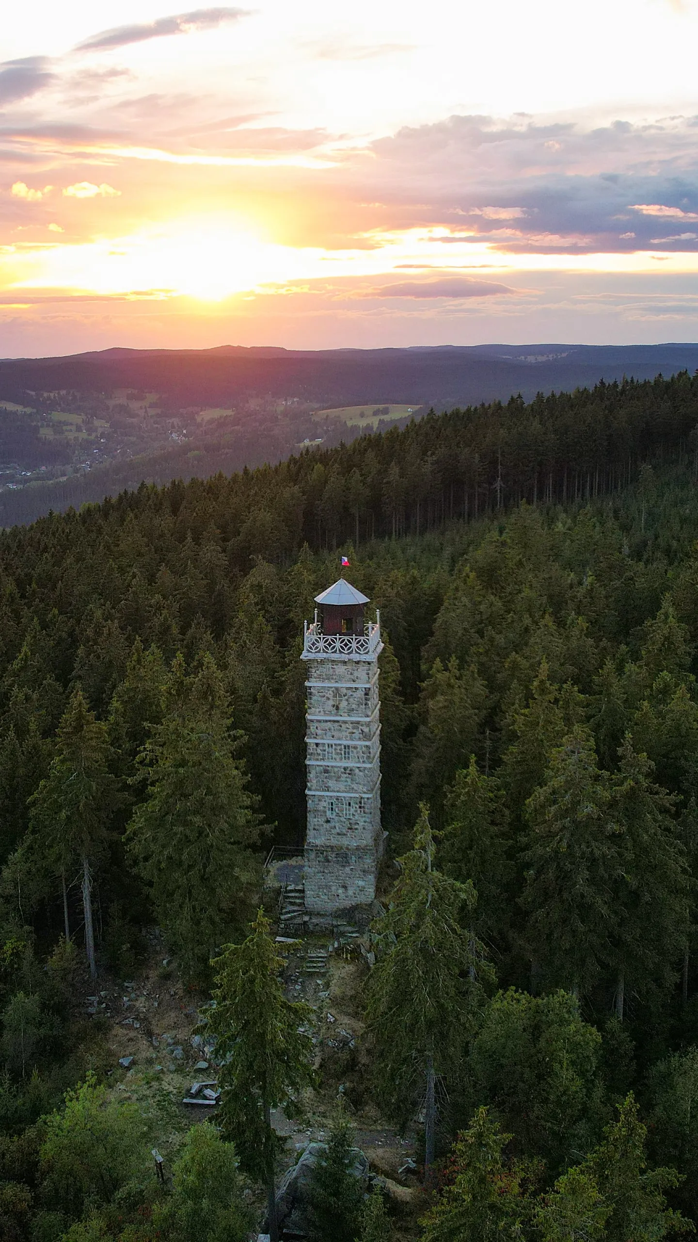 The stone Pajndl lookout tower among spruces in the Ore Mountains, the setting sun behind it