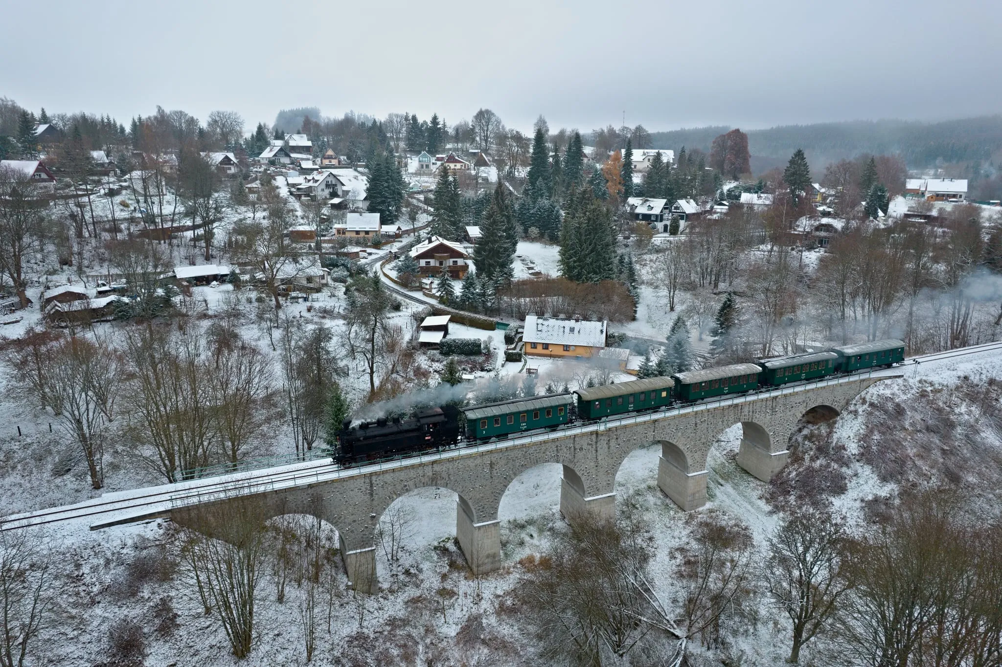 The St Nicholas steam train crossing a stone viaduct by a snowy village