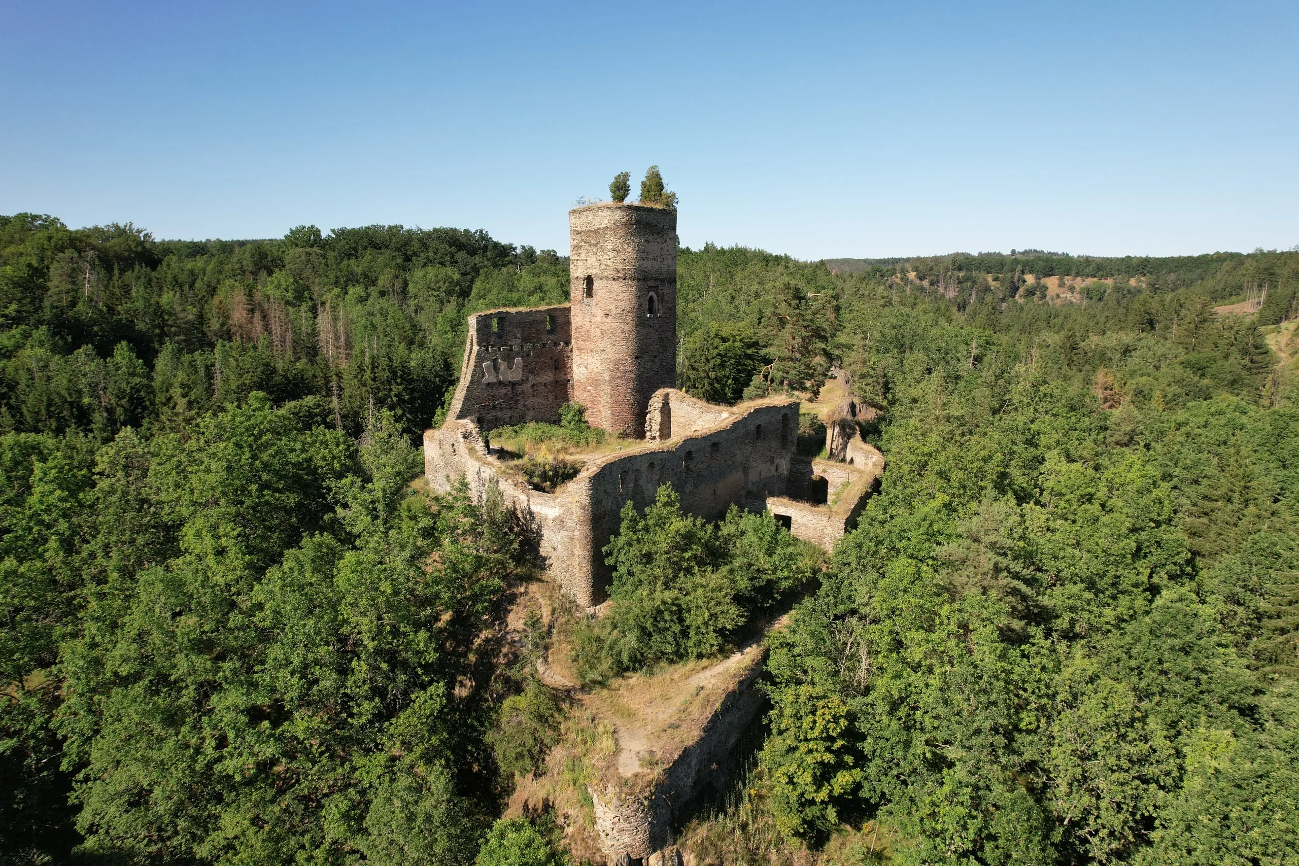 The ruins of Gutštejn Castle with a round tower on a rock above the forests