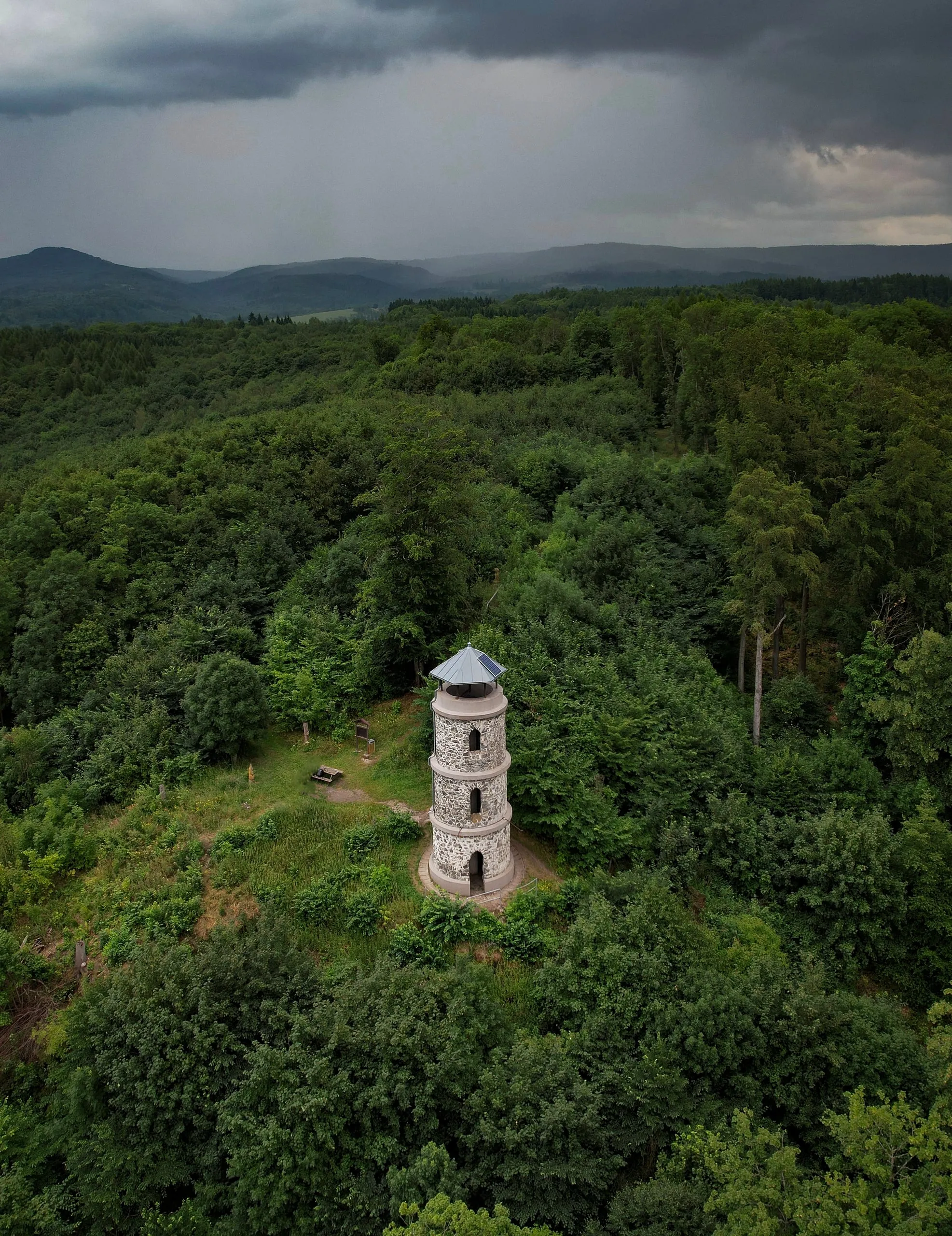 The stone Bučina lookout tower in a clearing, a storm approaching over the hills