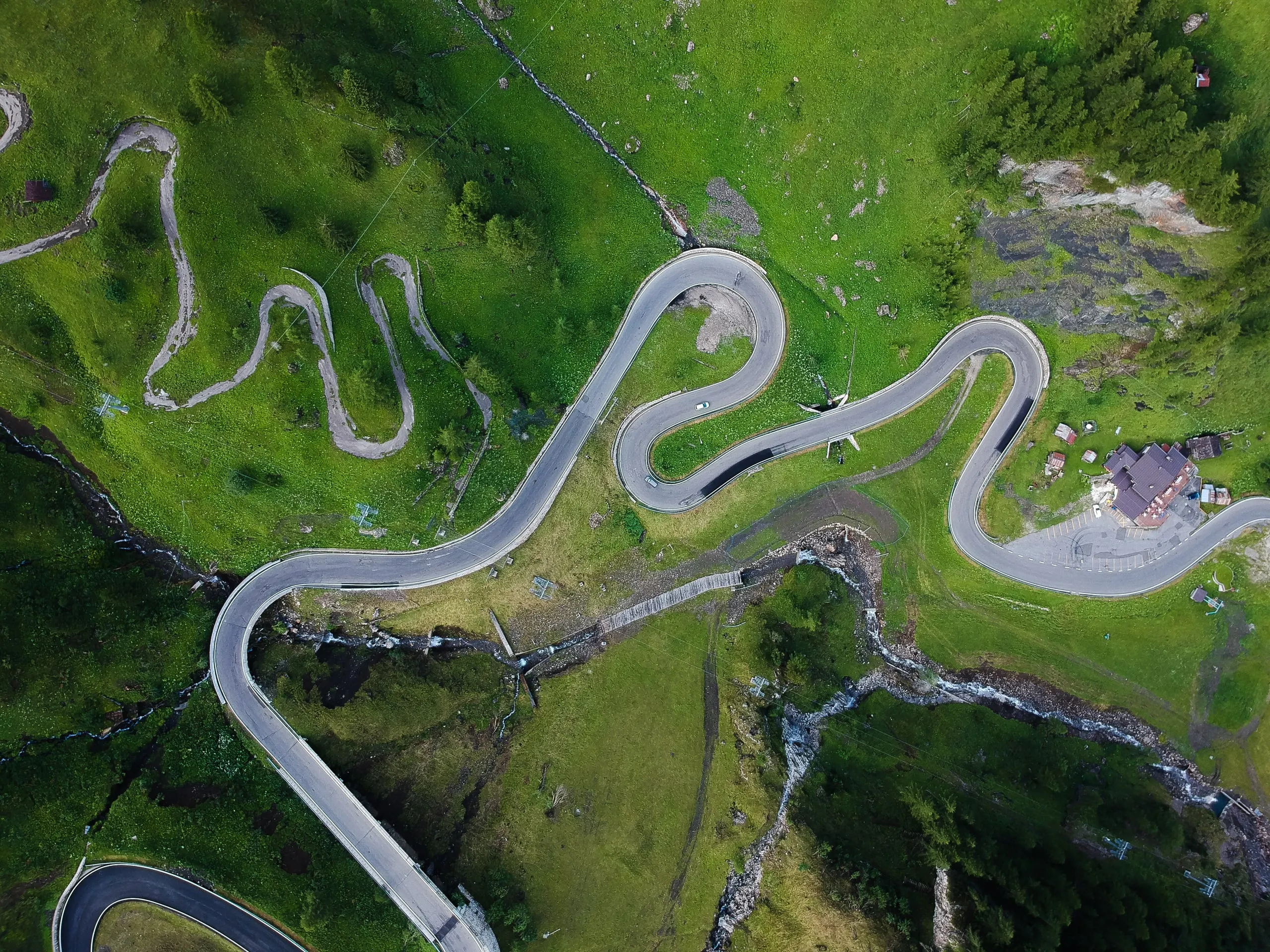 Hairpin bends of a mountain road between pastures in Italy, from straight above