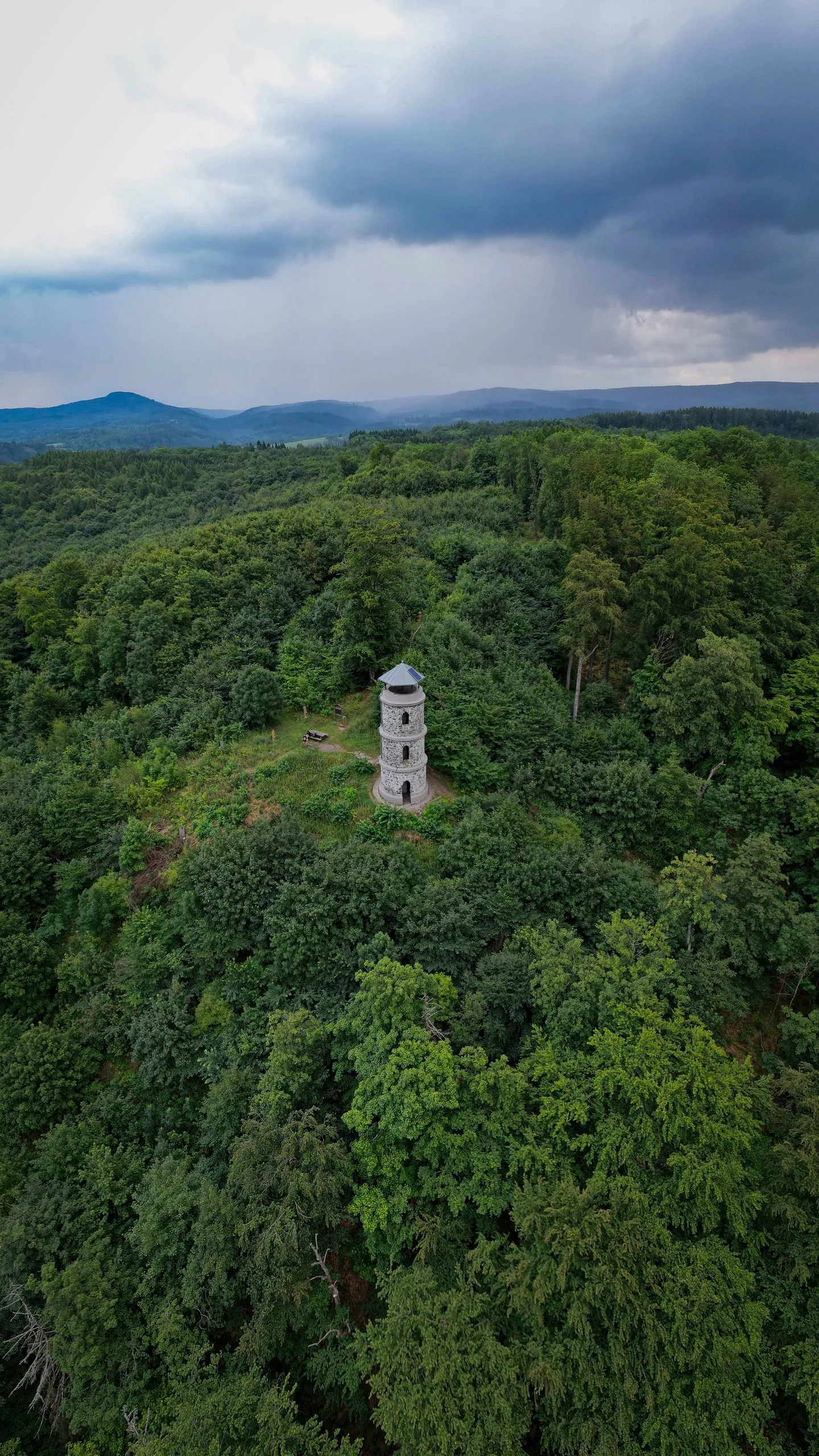 A stone lookout tower in the middle of a deciduous forest under storm clouds