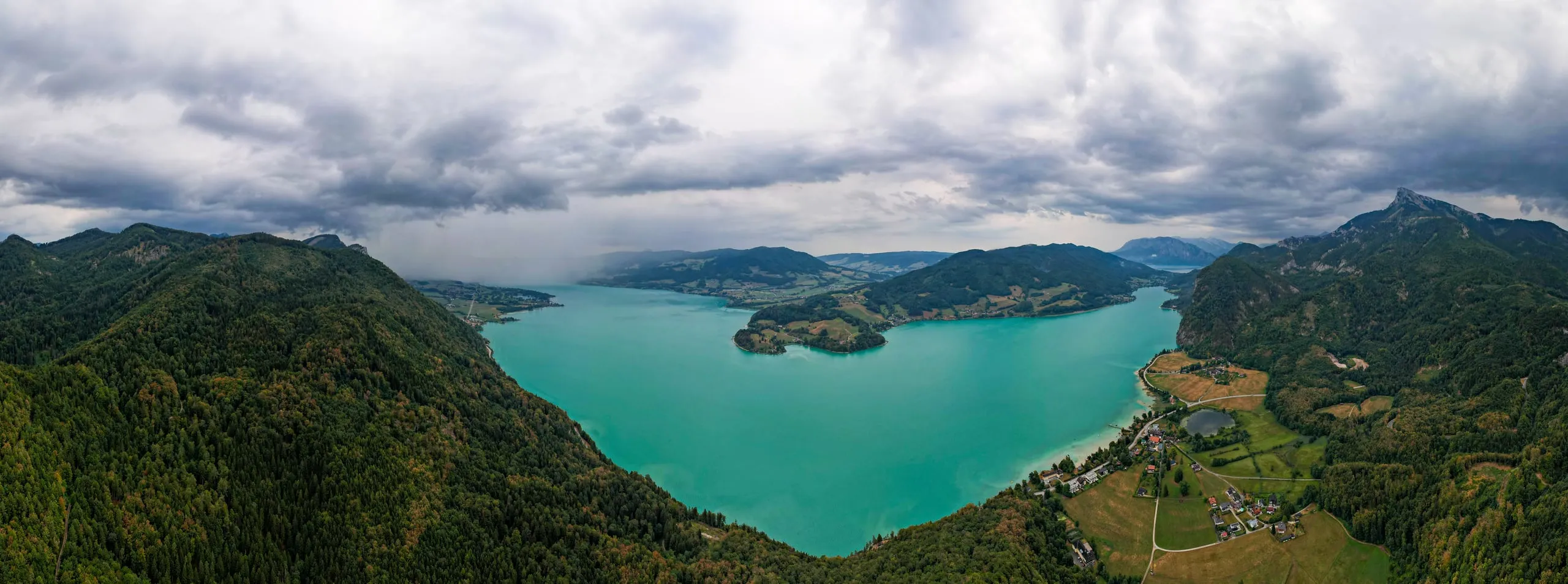 Panorama of the turquoise Mondsee with a peninsula under an overcast sky