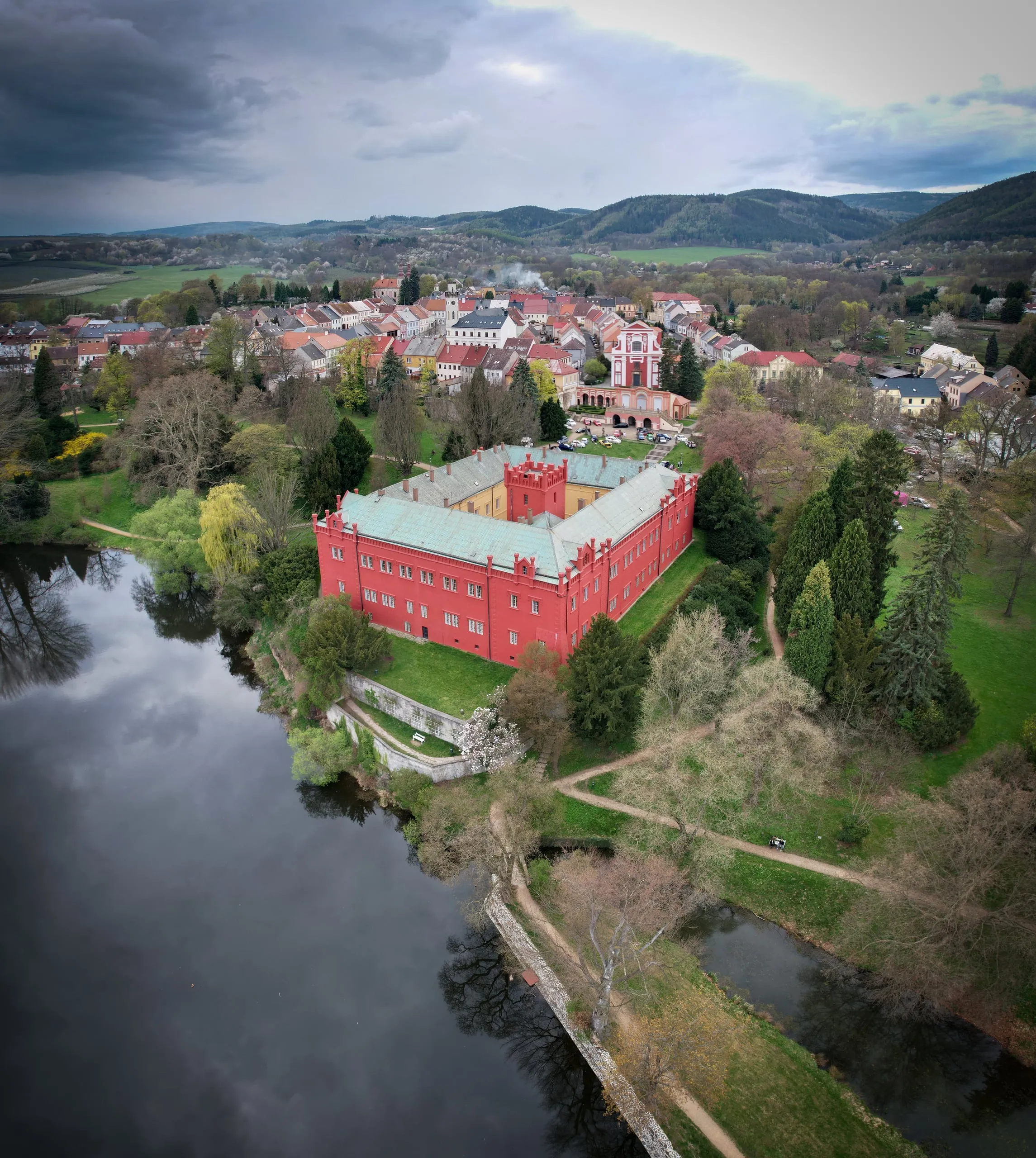 The red château in Klášterec with a courtyard on a river bank, the town and hills behind it