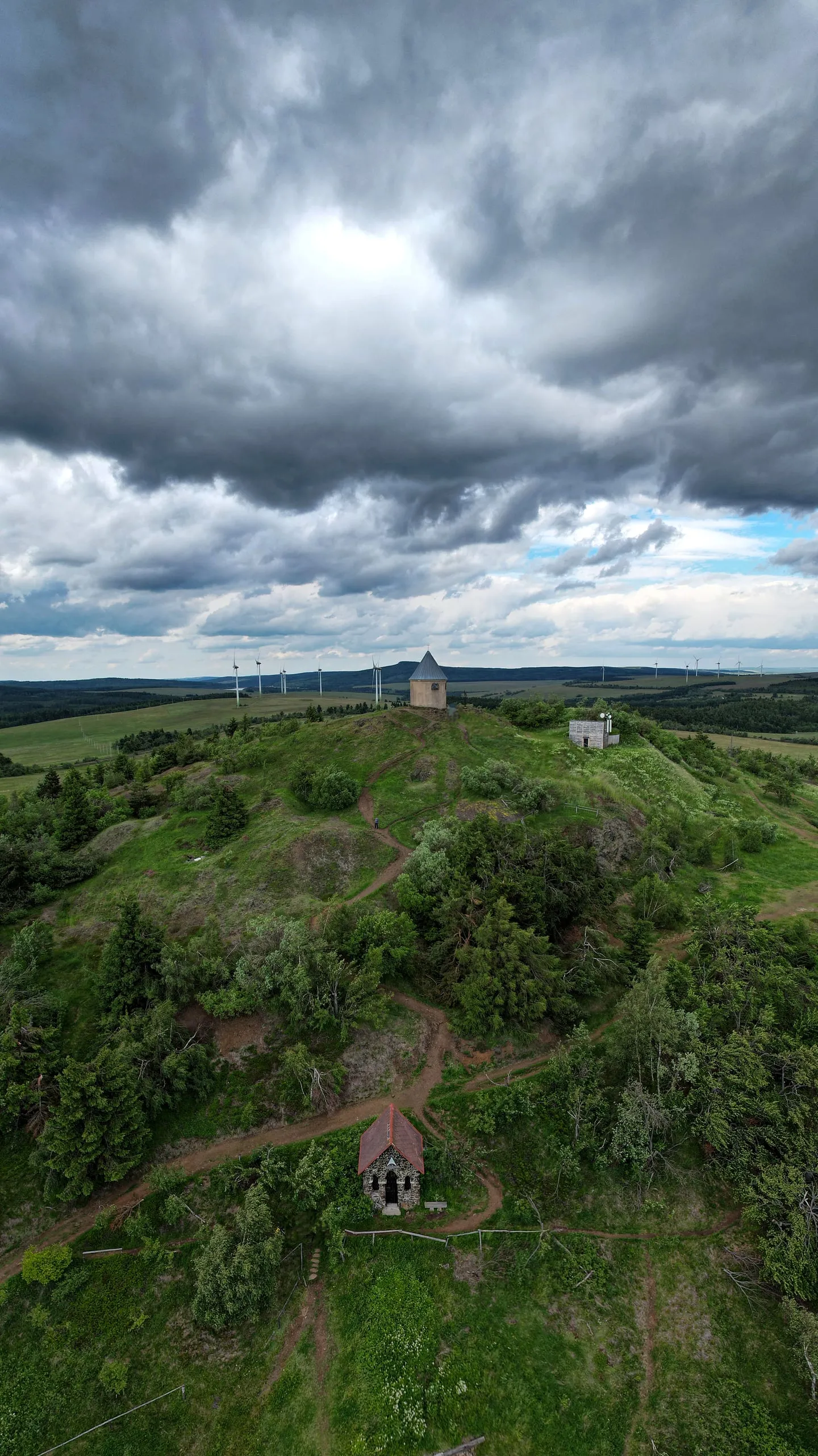The grassy hill of Mědník near Měděnec with a chapel on its slope under heavy clouds