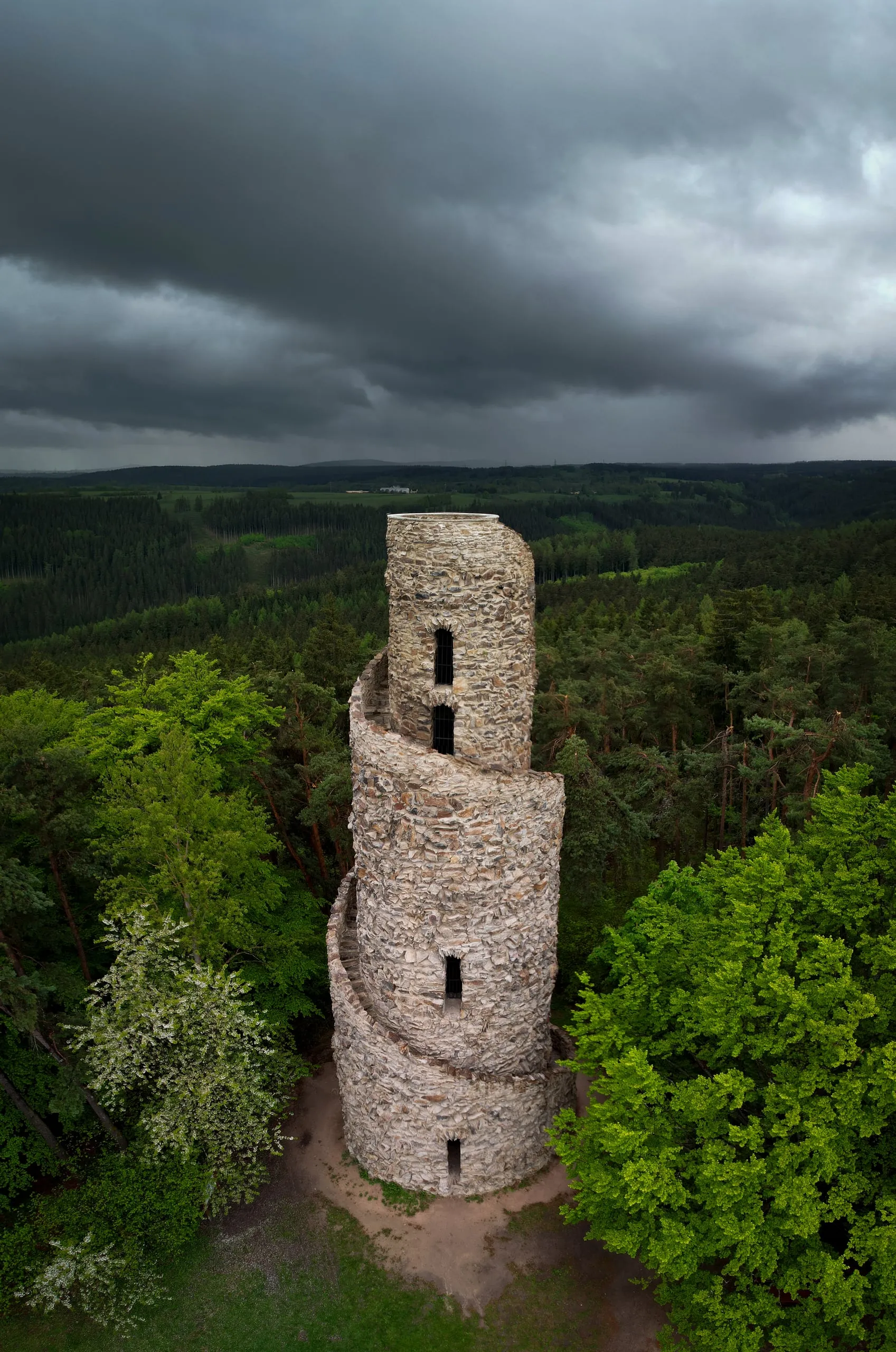 The stone Krásno lookout tower with its spiral staircase above the forests, storm clouds overhead