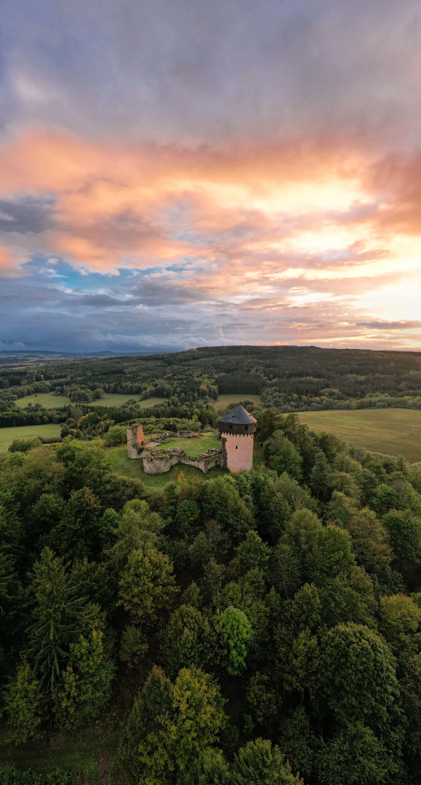 A castle ruin with a tower above the forest, the sky after sunset